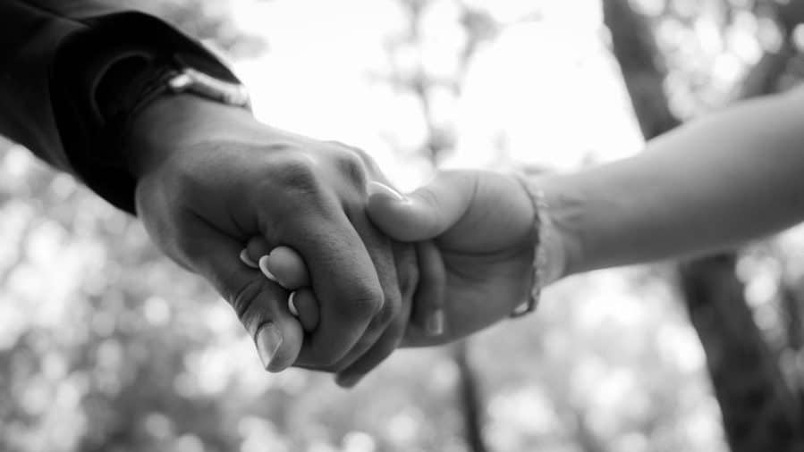B&W photo of wedding couples hands. A black man's hand and a white woman's hand clasp each other.