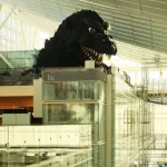 Iconic Godzilla statue inside a bustling, modern airport terminal with a high ceiling.