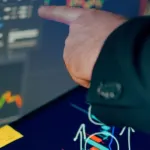 A business professional examines financial charts on a tablet and monitor for investment strategy.