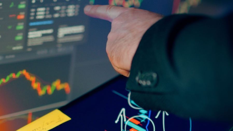 A business professional examines financial charts on a tablet and monitor for investment strategy.