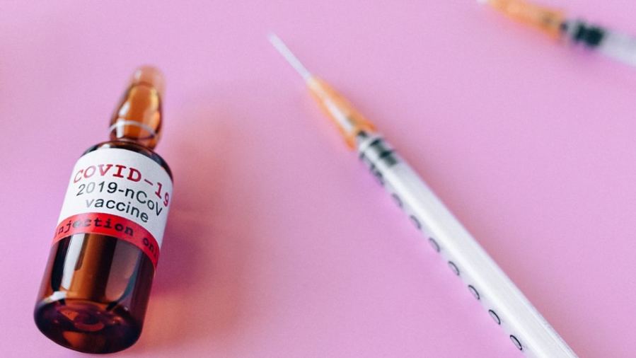 Close-up of a COVID-19 vaccine vial and syringes against a pink background, symbolizing healthcare.