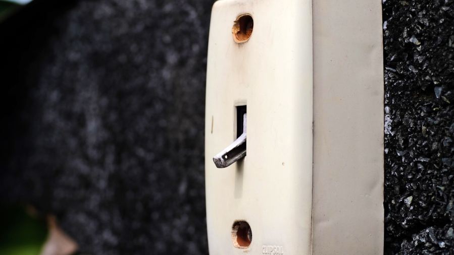 Close-up of a vintage wall-mounted electrical switch on a concrete wall with greenery.