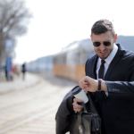 A businessman in a suit checks his watch while rushing on a sunny day in the city.