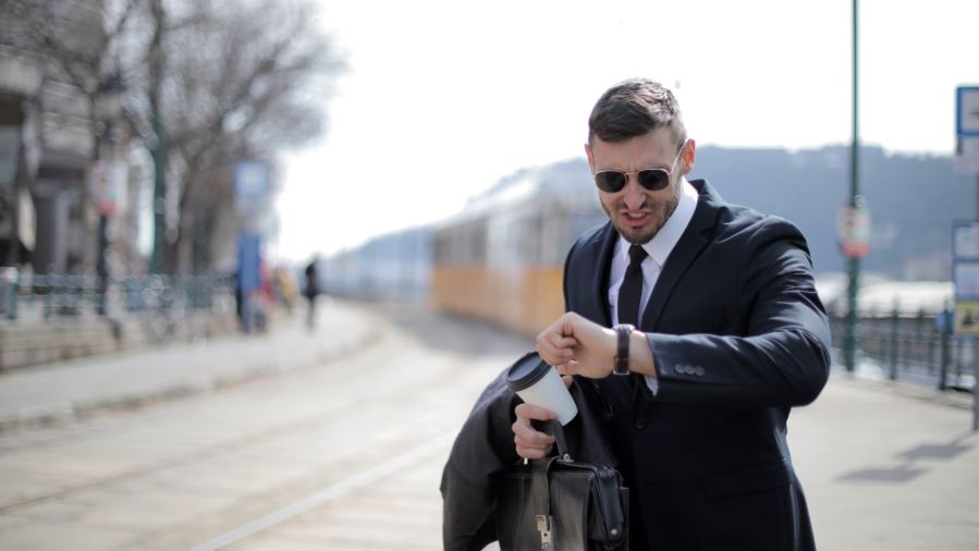 A businessman in a suit checks his watch while rushing on a sunny day in the city.