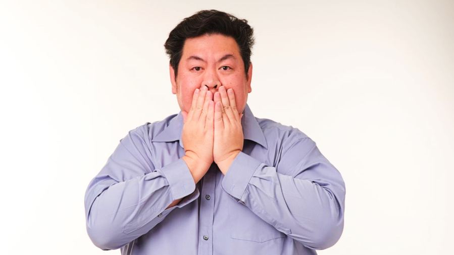 Portrait of a man covering his mouth with his hands, expressing surprise, against a neutral background.