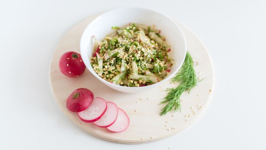 A healthy vegan salad with buckwheat, radish, and dill garnished with sesame seeds.