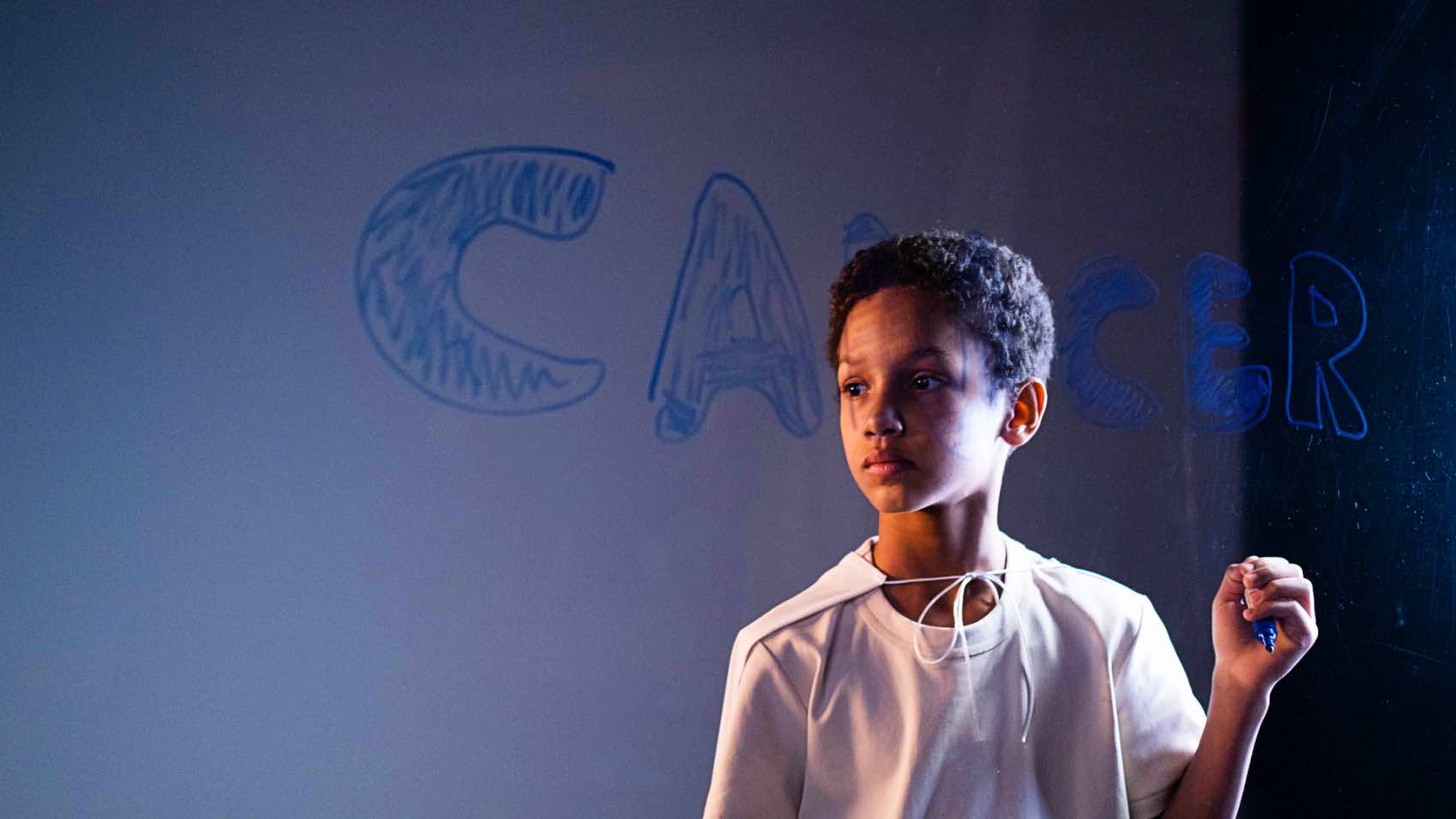 A young boy stands indoors holding a marker, raising cancer awareness.