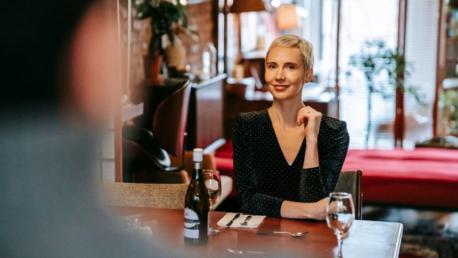 A happy woman enjoying a romantic dinner in a cozy restaurant setting, featuring wine and warm decor.
