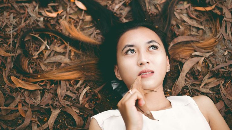 Thoughtful woman lying on leaves, gazing upwards with autumn background.