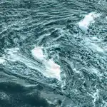 A mesmerizing aerial view of swirling ocean water patterns with whitecaps.