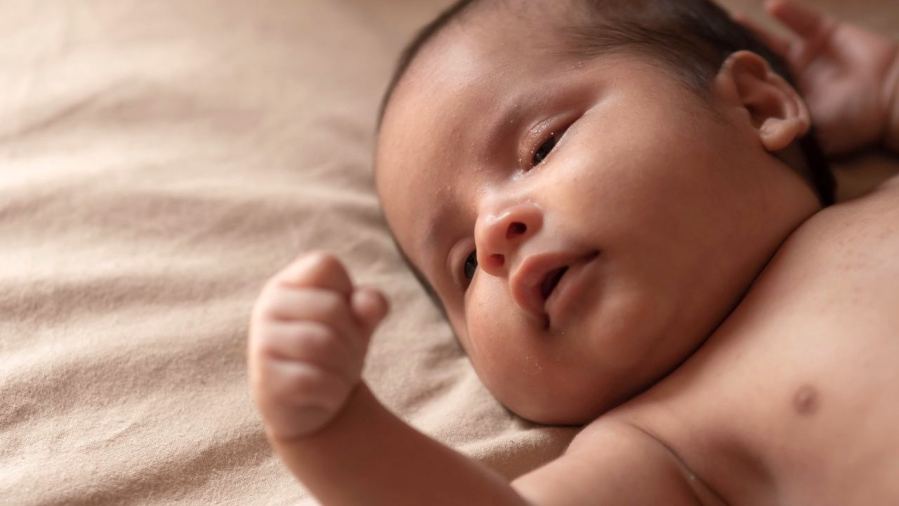 Adorable baby lying on a soft beige blanket in natural light.