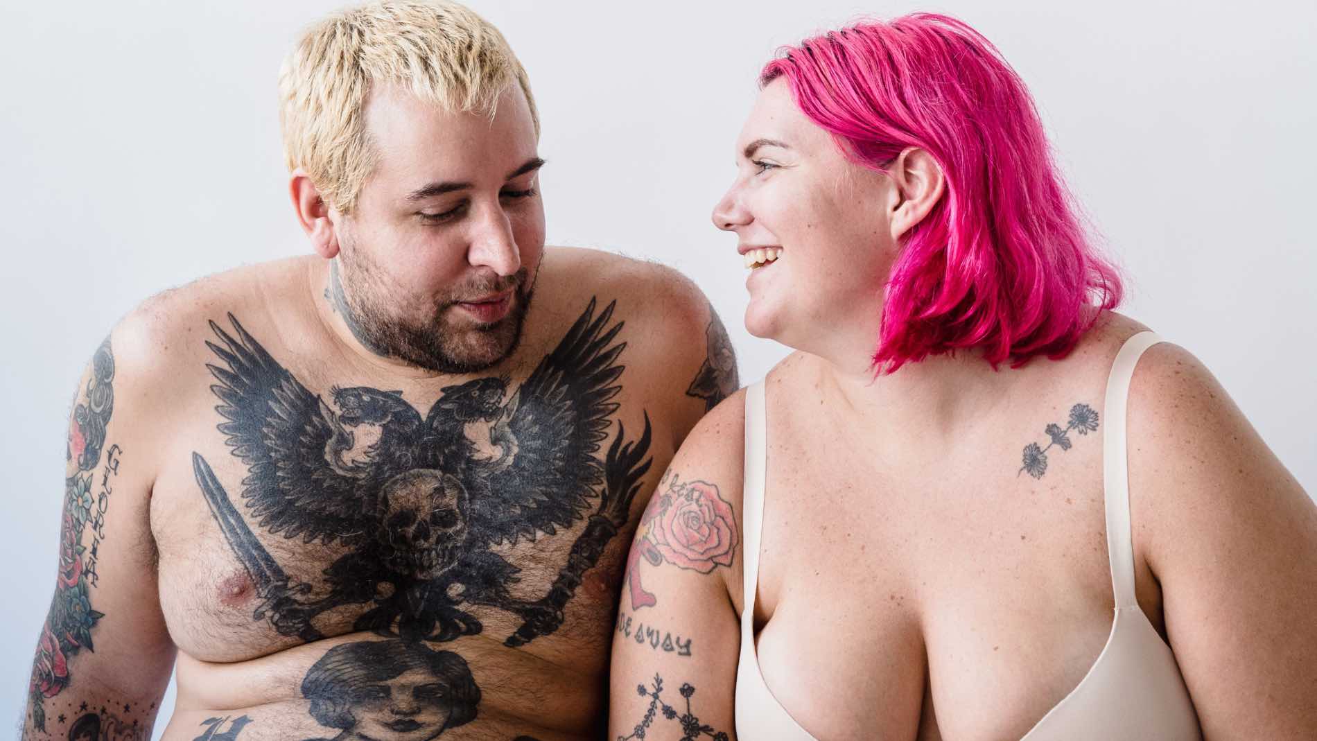 Smiling tattooed couple celebrating body positivity on a white background.