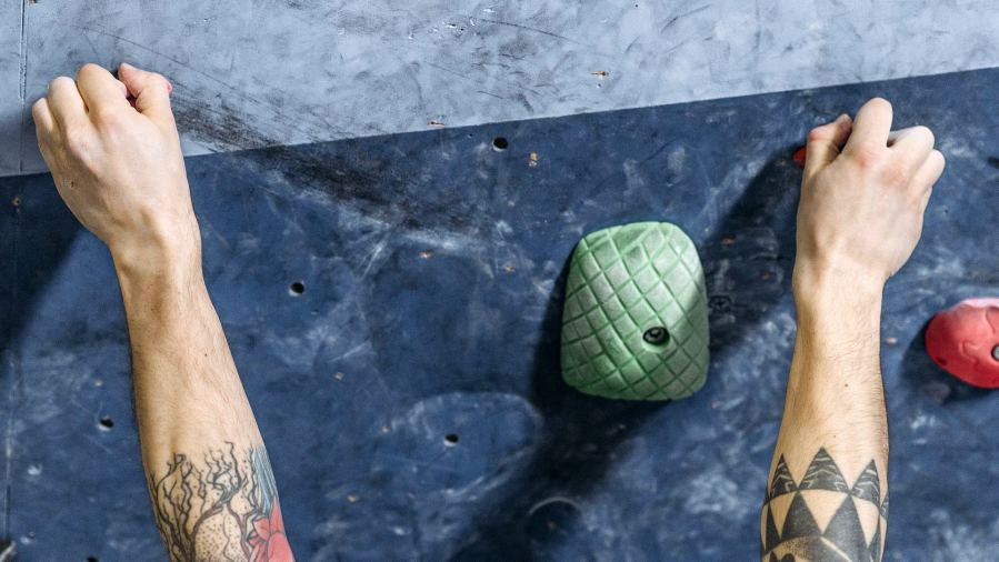 Close-up of a climber's hands gripping jugs on an indoor bouldering wall.
