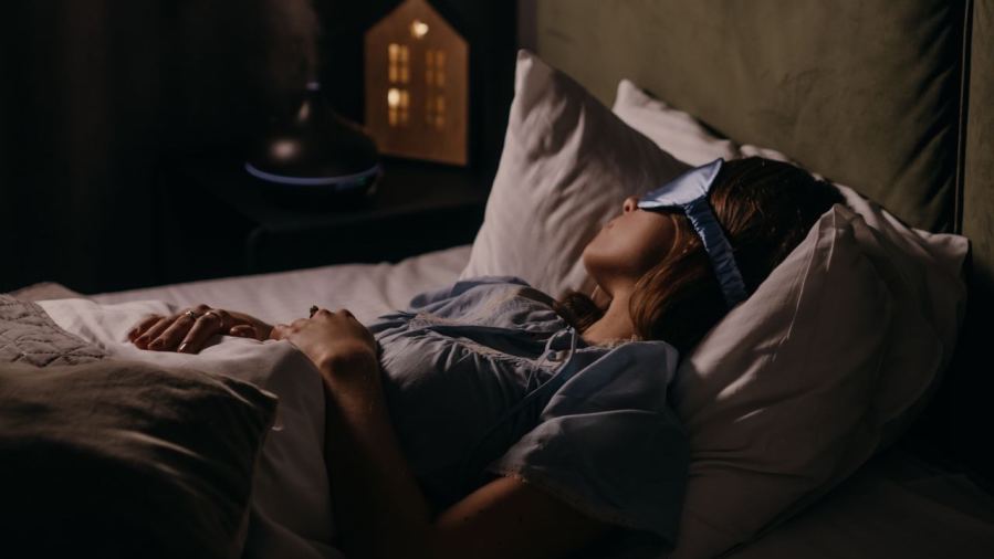A woman peacefully sleeping with an eye mask in a dimly lit bedroom, capturing a serene bedtime atmosphere.