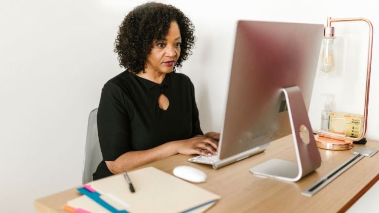 Woman in black attire working on a desktop computer in an office environment.