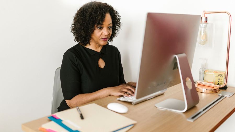 Woman in black attire working on a desktop computer in an office environment.