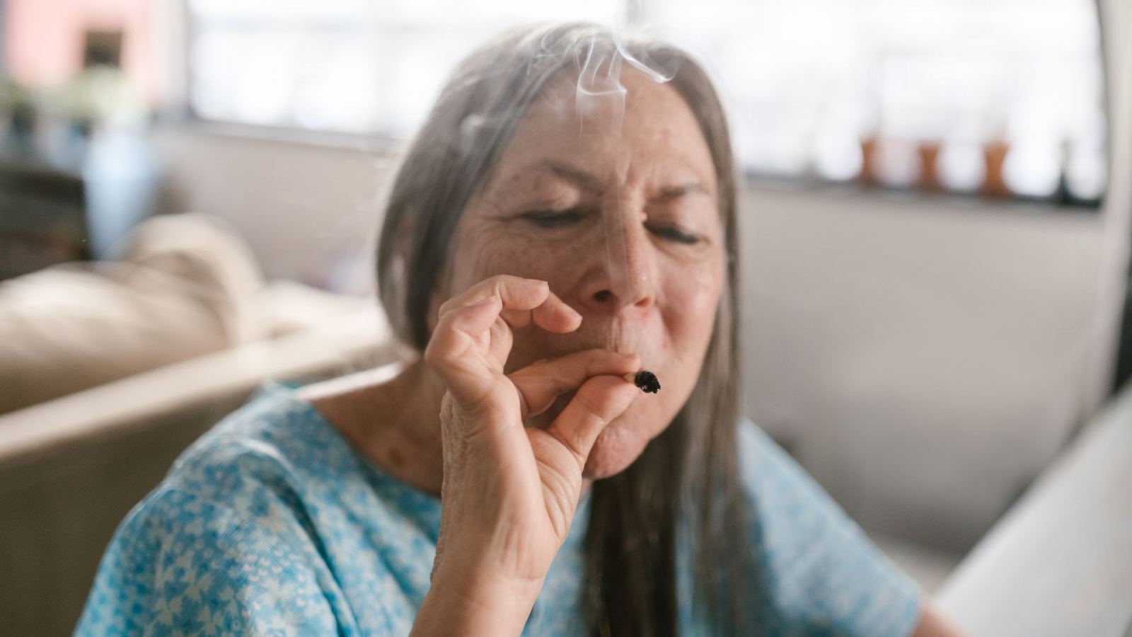 Elderly woman enjoying a marijuana joint, embracing relaxation indoors.
