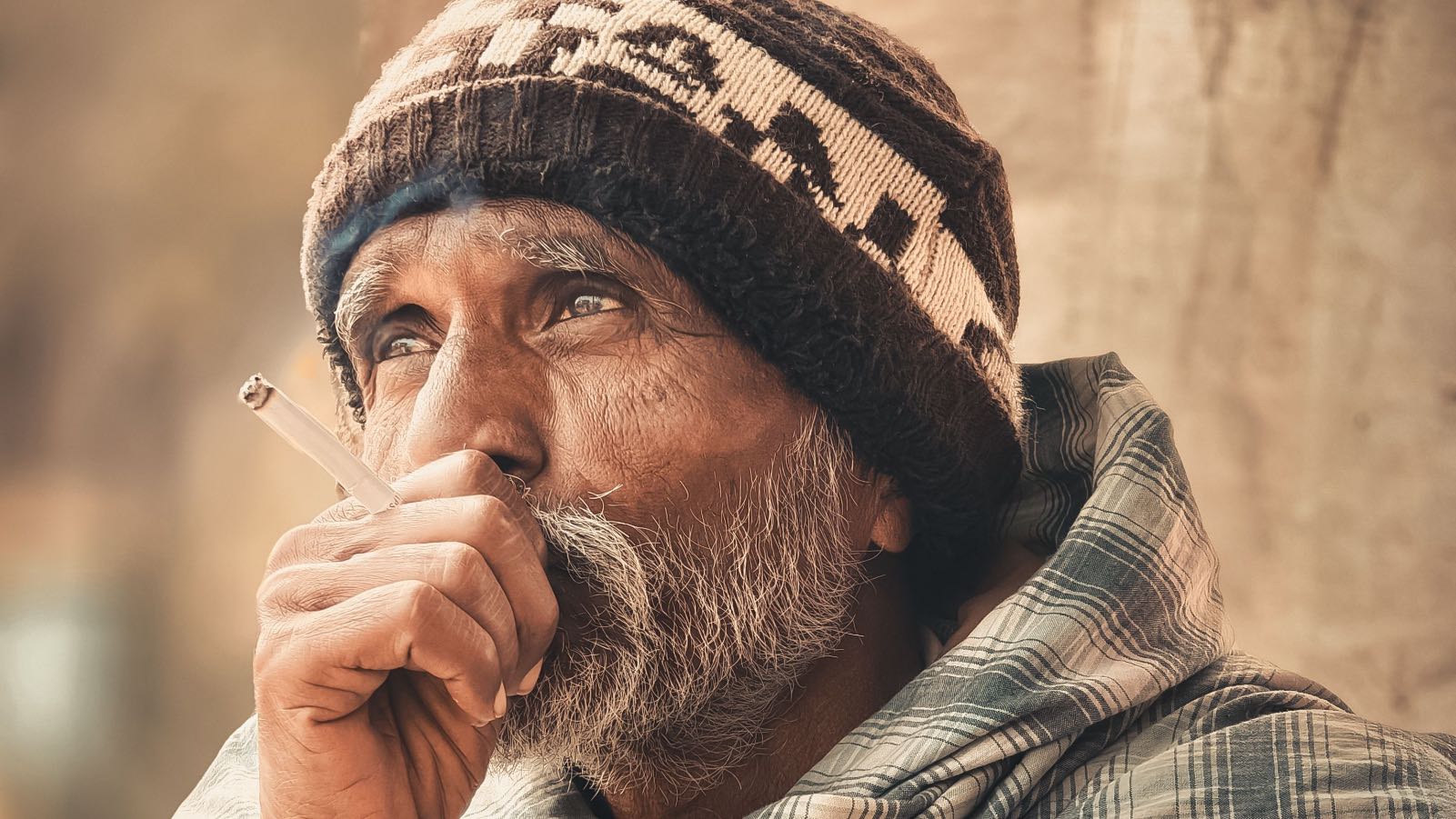 Portrait of an elderly man in Mirjapur, India, smoking while wearing winter attire, capturing a reflective moment.
