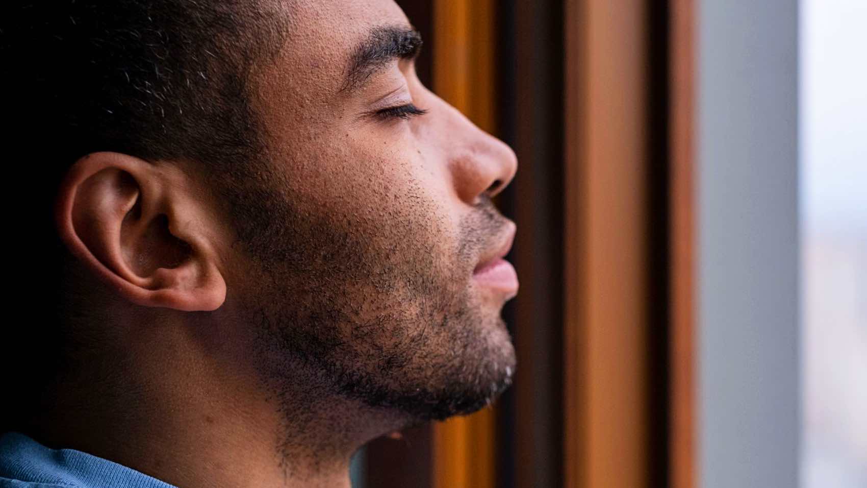Side profile of a man with closed eyes enjoying a calm moment by the window.