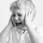 Black and white portrait of a sad child covering ears, expressing frustration.
