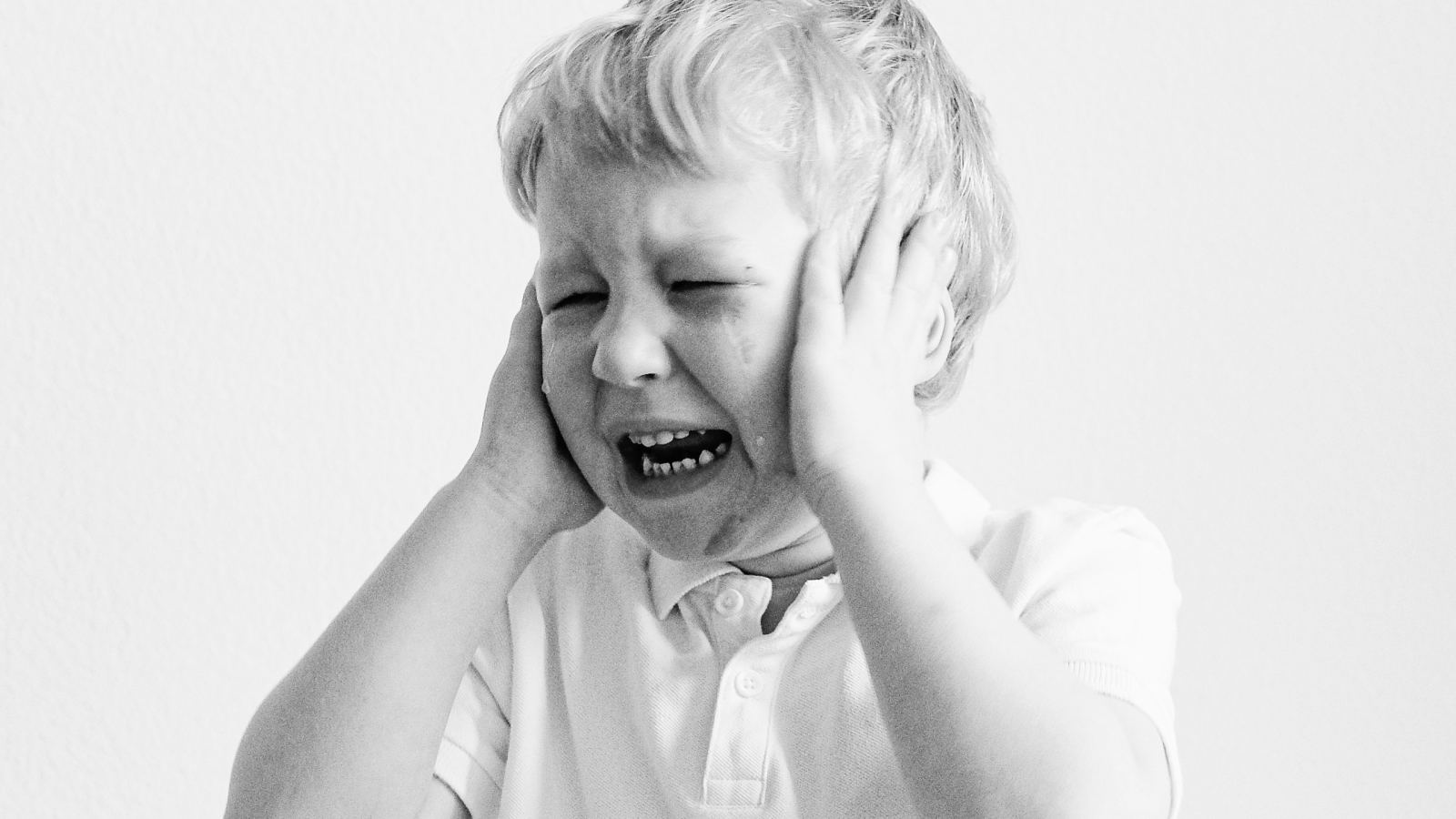 Black and white portrait of a sad child covering ears, expressing frustration.