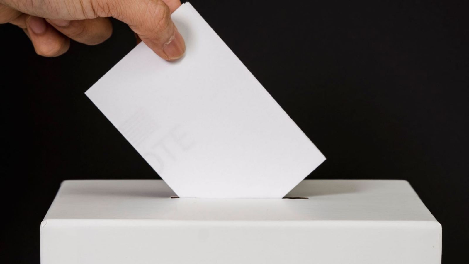 A person placing a ballot into a voting box, symbolizing democratic participation and civic duty.