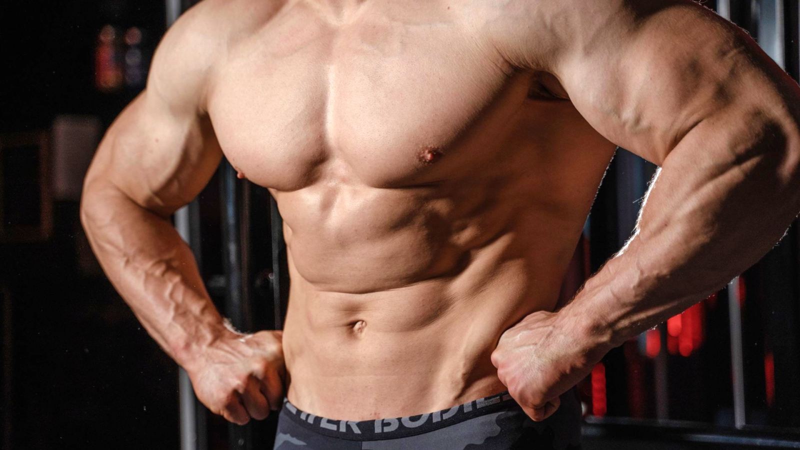 Detailed image of a muscular male torso flexing in a gym setting, emphasizing strength.