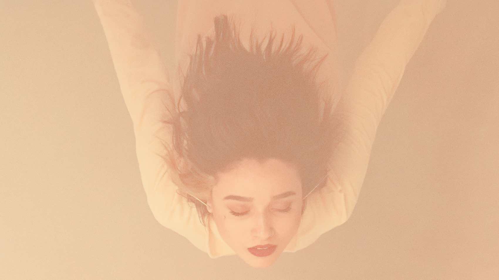 Artistic photo of a woman floating underwater in soft hues.