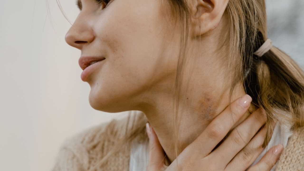 Side view of a woman touching her neck, appearing thoughtful and slightly concerned.