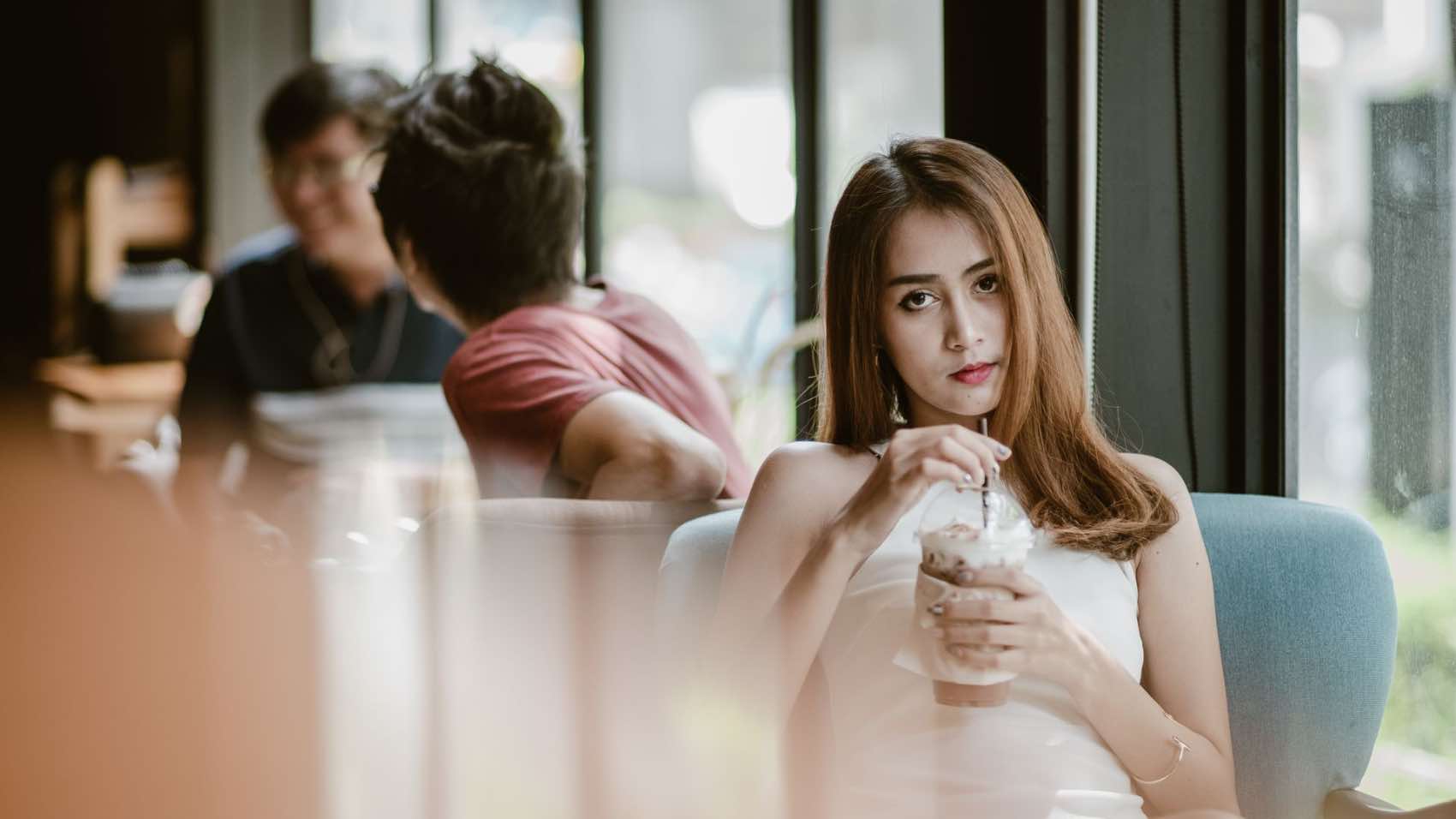 Young woman in a white dress relaxing with a cold drink in a modern cafe.