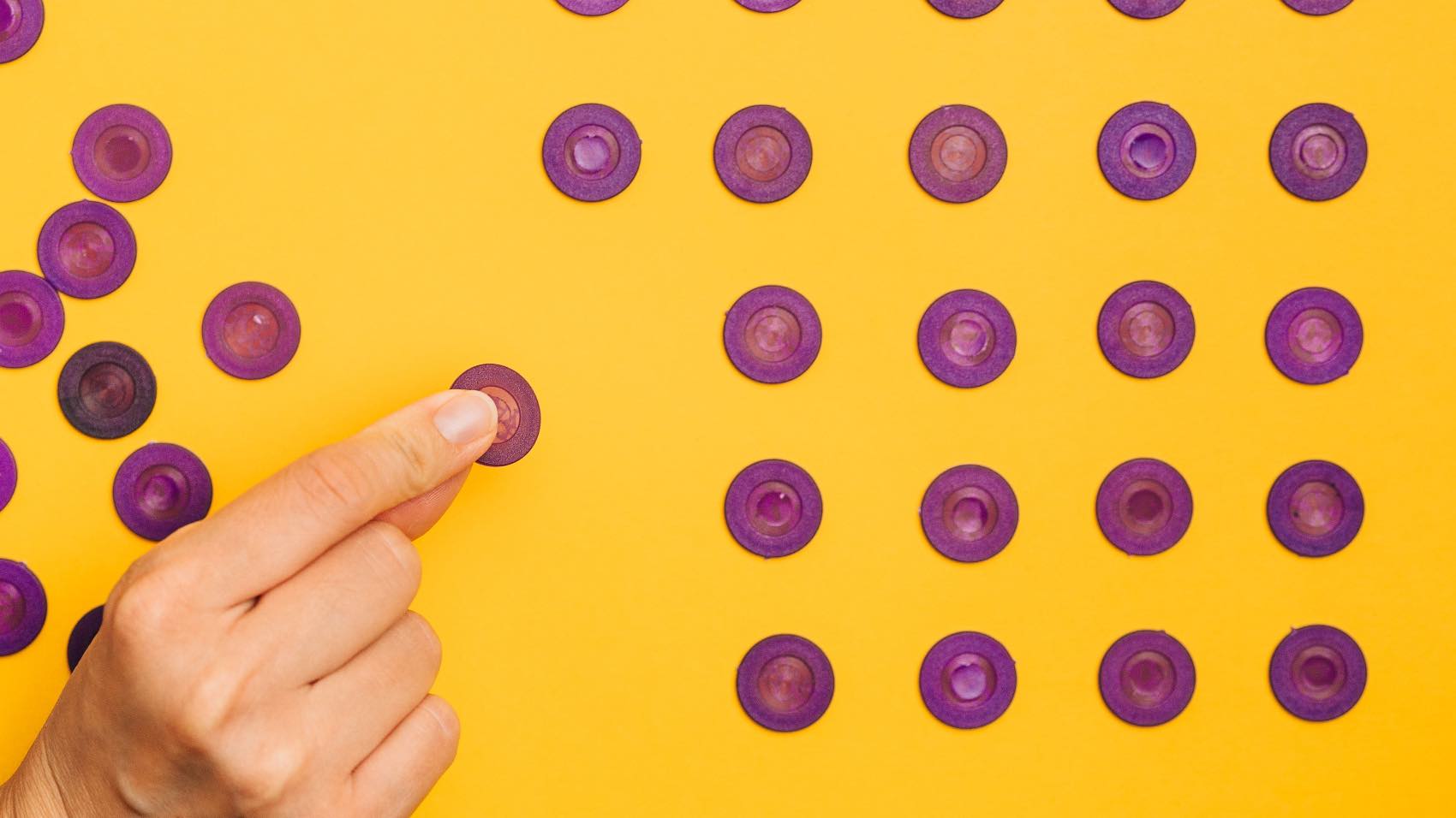 Close-up of a hand arranging purple tokens in a pattern on a vibrant yellow background.