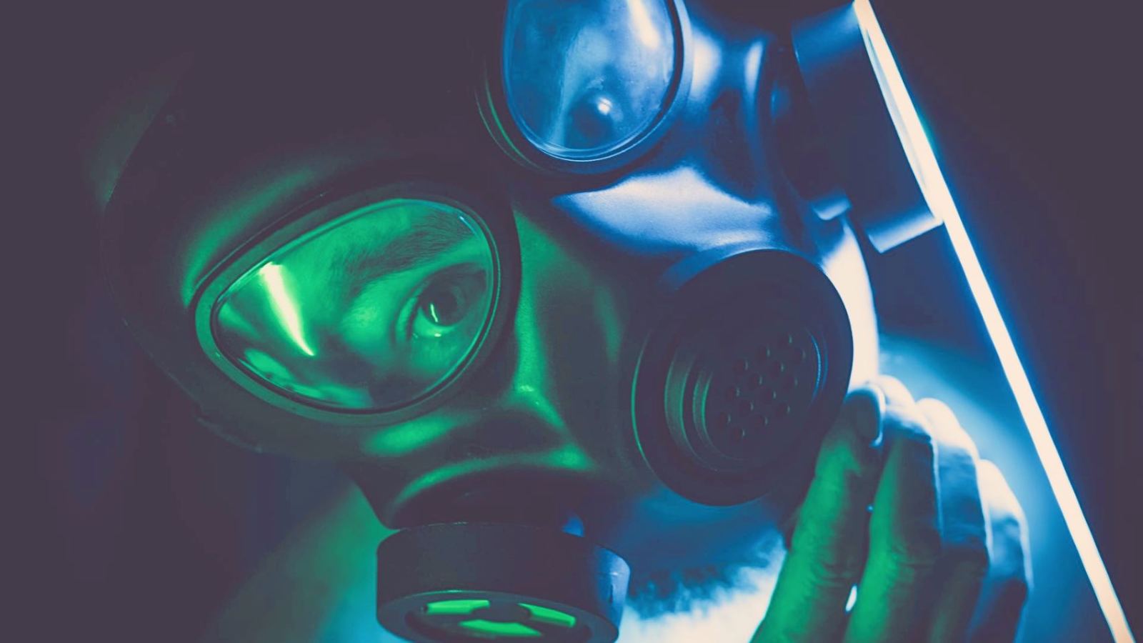 A moody, mysterious portrait featuring a person wearing a gas mask in eerie lighting.