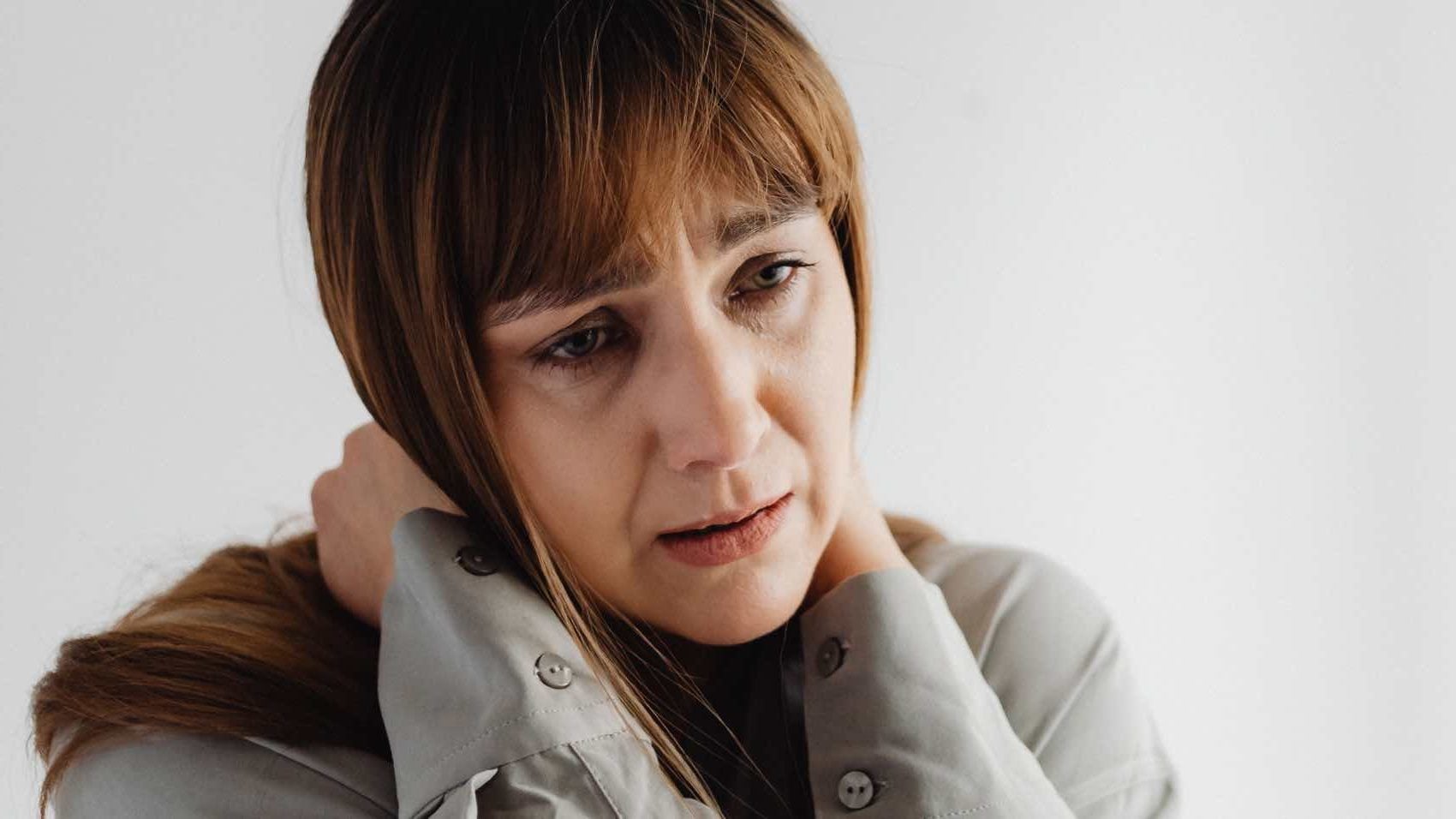 Portrait of a woman in gray with hands on neck, expressing worry and sadness.