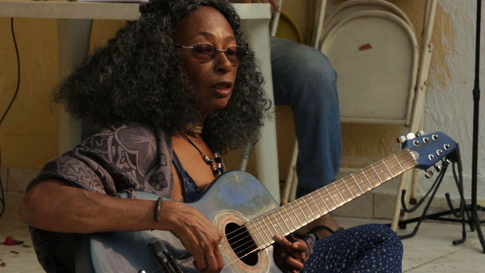 A woman performs outdoors with an acoustic guitar, casual and relaxed.
