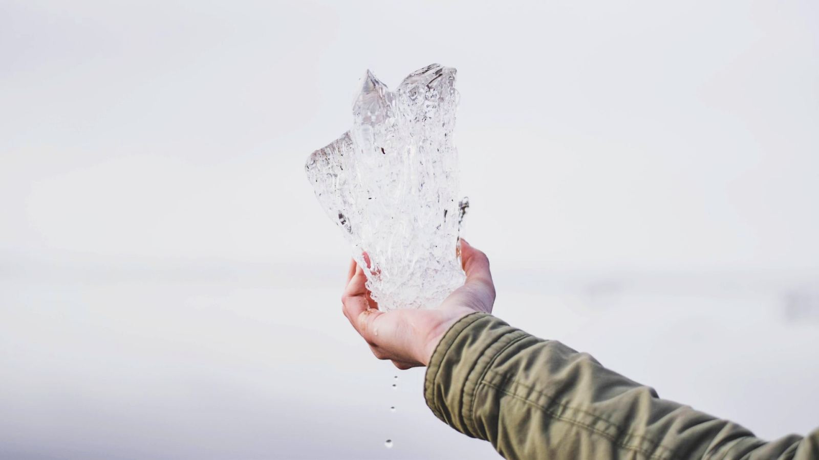 A hand holding a large piece of clear ice against a light background.